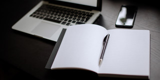 Laptop, Notizbuch und Smartphone Eingeschalteter Laptop, Smartphone und Notizbuch mit Stift auf einem Tisch liegend.